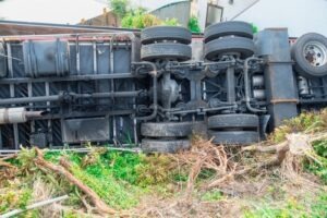 Overturned commercial truck lying on its side near vegetation after a roadway crash.