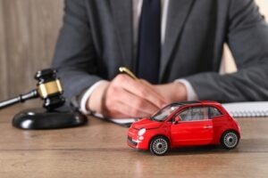 A small red toy car sits beside a gavel on a lawyer’s desk, symbolizing legal representation in car accident cases.