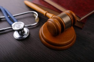 A wooden gavel rests beside a stethoscope and legal books on a dark wooden desk, representing medical and legal matters.