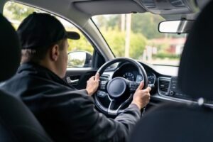Rideshare driver in a black cap holding the steering wheel while driving through a suburban neighborhood.