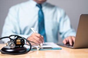 Close-up of a lawyer working at a desk with a stethoscope and gavel in the foreground, symbolizing medical malpractice or personal injury law.