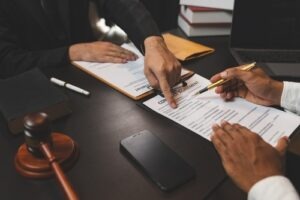 Lawyers reviewing and signing legal documents at a desk with a gavel, contract papers, and a smartphone visible.