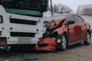 A red sedan with severe front-end damage after colliding with a large white truck on a road, showing the aftermath of a serious car accident.