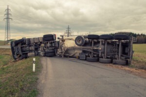 Overturned semi-truck blocking a rural road with cloudy skies and power lines in the background.