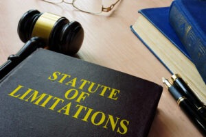 Close-up of a legal book titled “Statute of Limitations” beside a judge’s gavel, pen, and eyeglasses on a wooden desk.