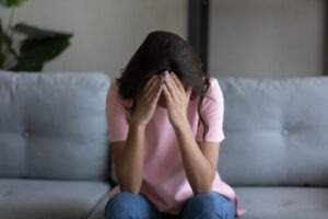 Woman sitting on a couch with her head in her hands, appearing distressed or grieving.