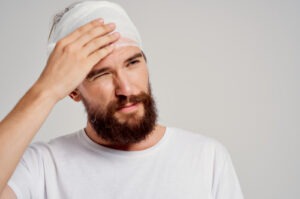 Man with a bandaged head touching his forehead and appearing to be in pain.