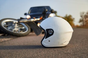 White motorcycle helmet on the road in front of a damaged motorcycle and vehicle after a collision.