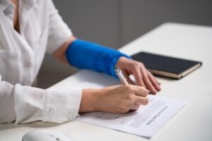 Injured worker with a blue arm brace filling out a workers’ compensation claim form at a desk.