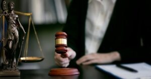Judge striking a gavel at a desk with a Lady Justice statue nearby.